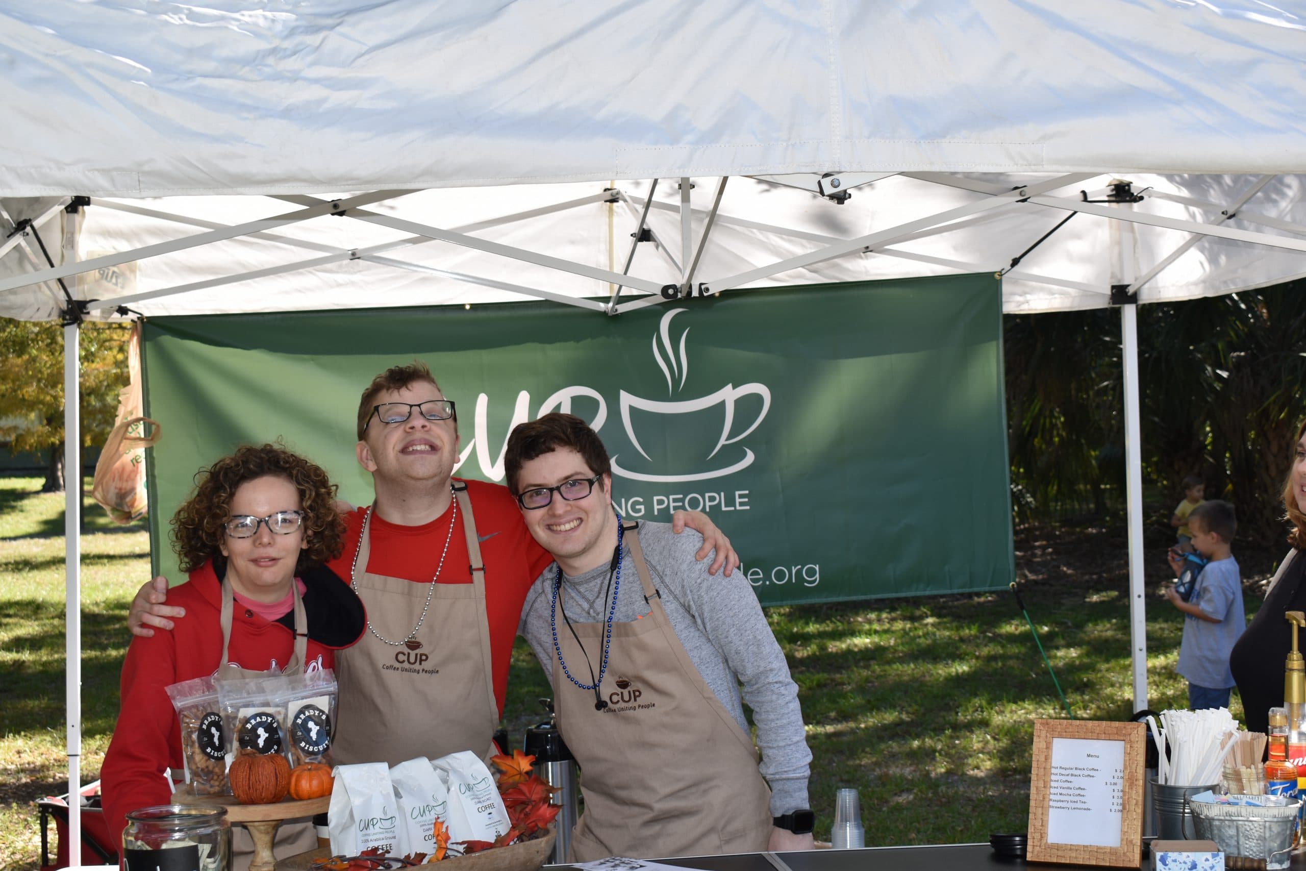 Three CUP team members posed under a white pop-up tent at an outdoor event